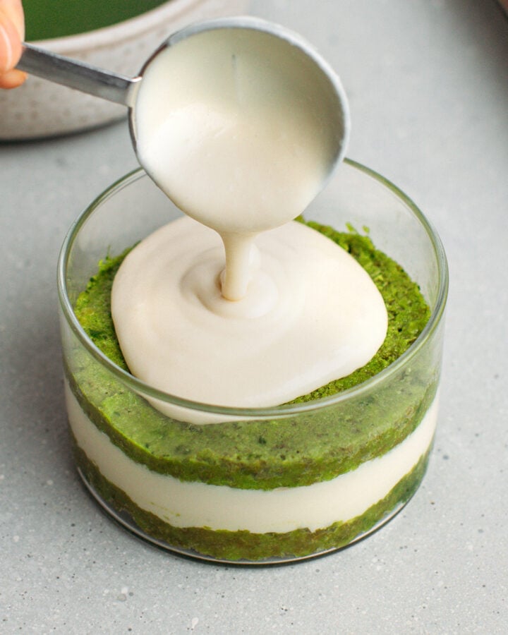Pouring the last layer of vanilla cream over a matcha sponge cake in a ramekin.