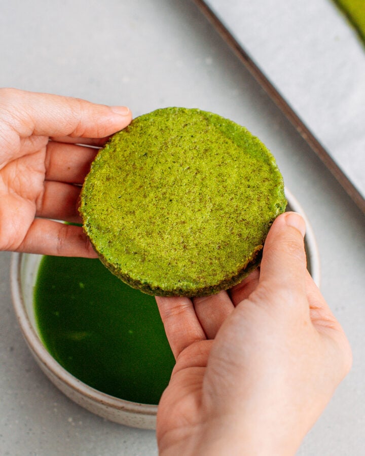 Holding a round of matcha sponge cake dipped in matcha tea.