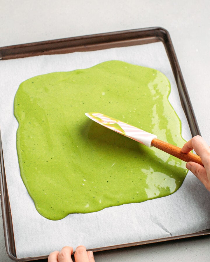 Spreading matcha sponge cake batter on a baking sheet.