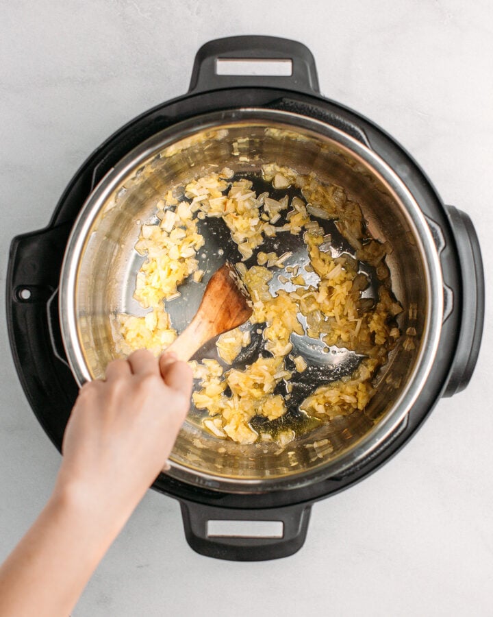 Stirring diced onions, garlic, and ginger in an Instant Pot.
