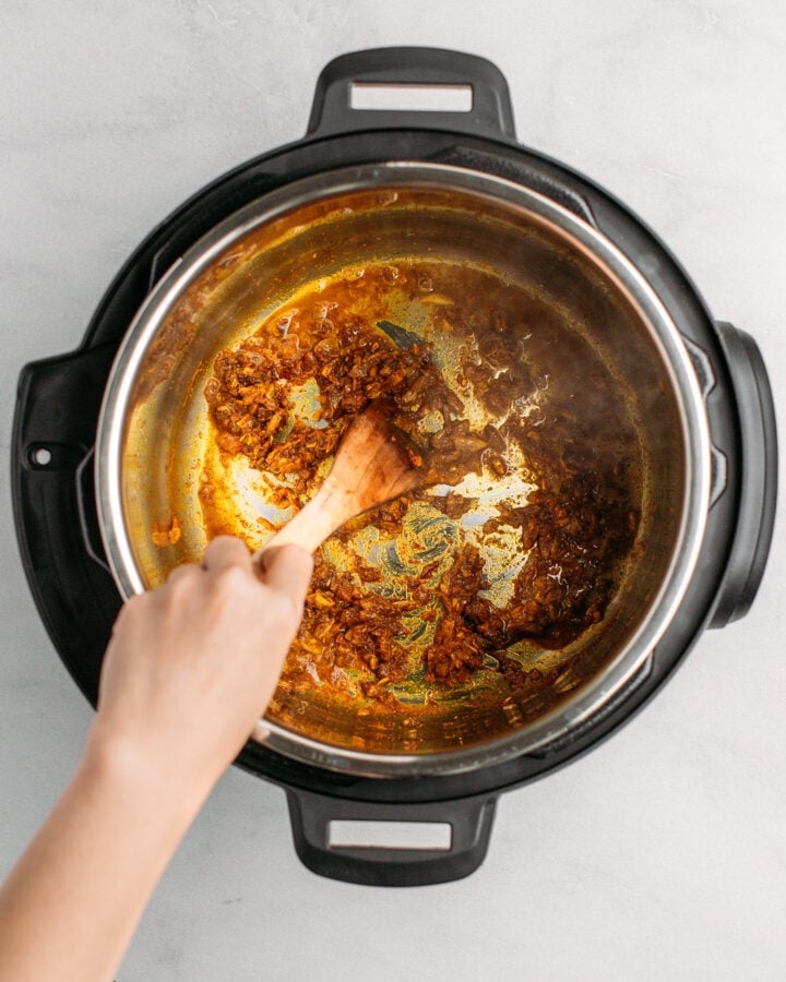 Stirring sautéed onions and garlic with spices in an Instant Pot.