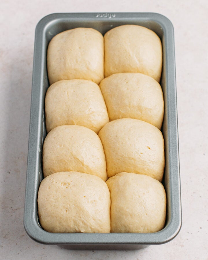 Fluffy brioche dough balls in a metal baking pan, ready for baking.
