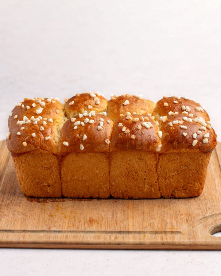 Fluffy brioche with sugar crystals on top, resting on a wooden cutting board.