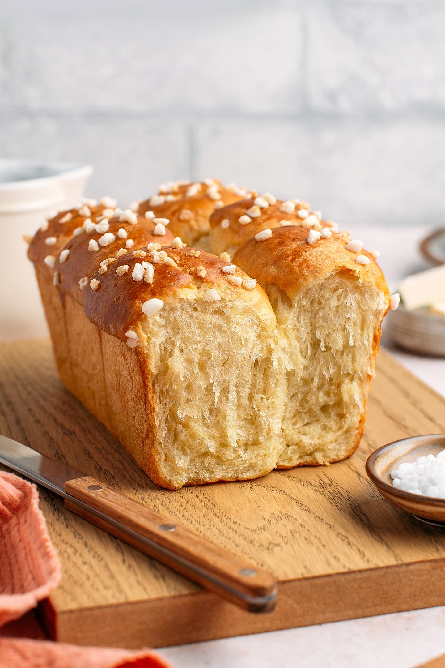Loaf of brioche topped with pearl sugar on a wooden board.