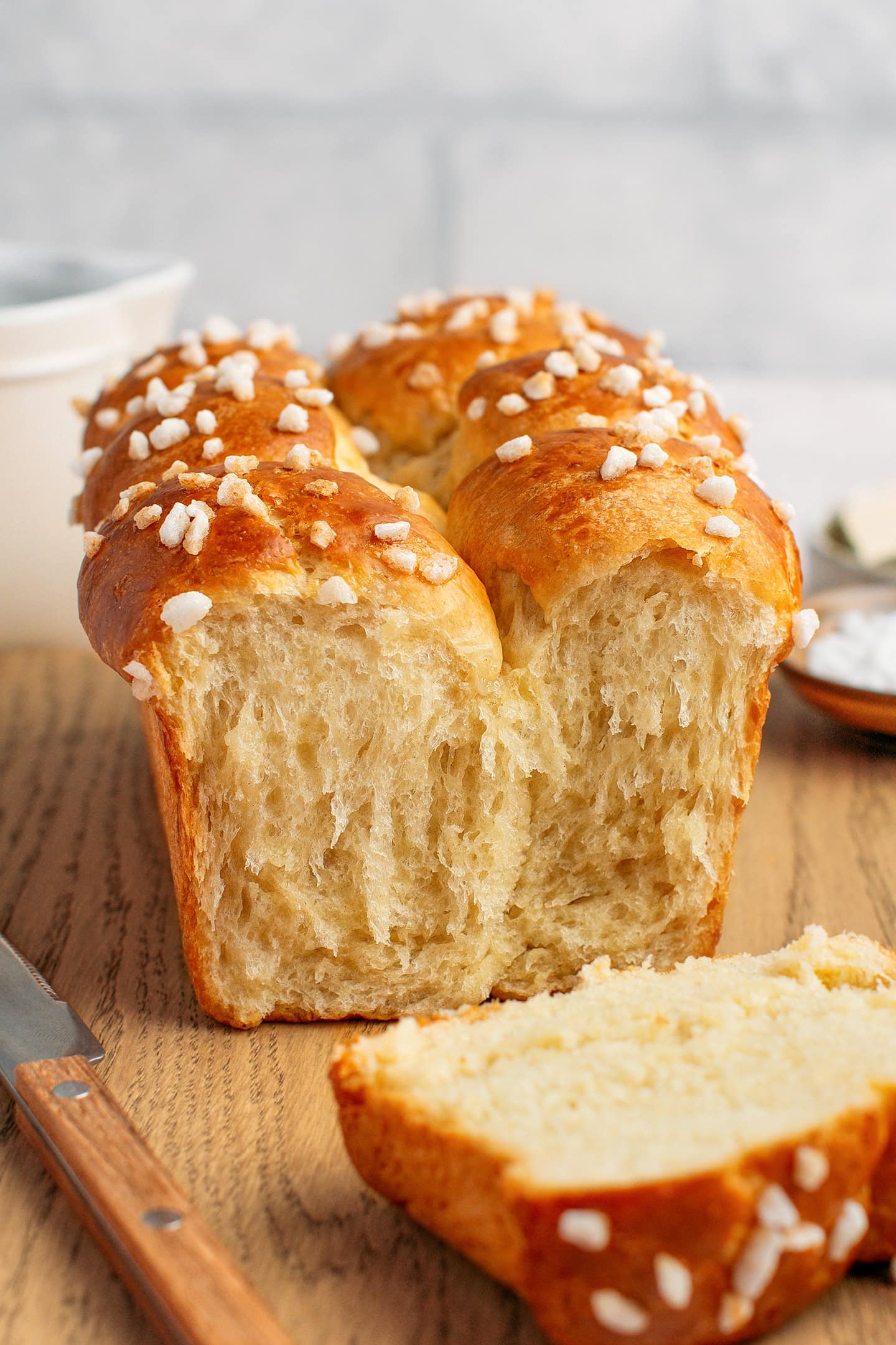 Vegan brioche topped with pearl sugar on a wood cutting board.