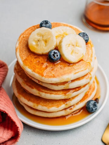 Stack of vegan pancakes drizzled with maple syrup and topped with banana slices and blueberries.