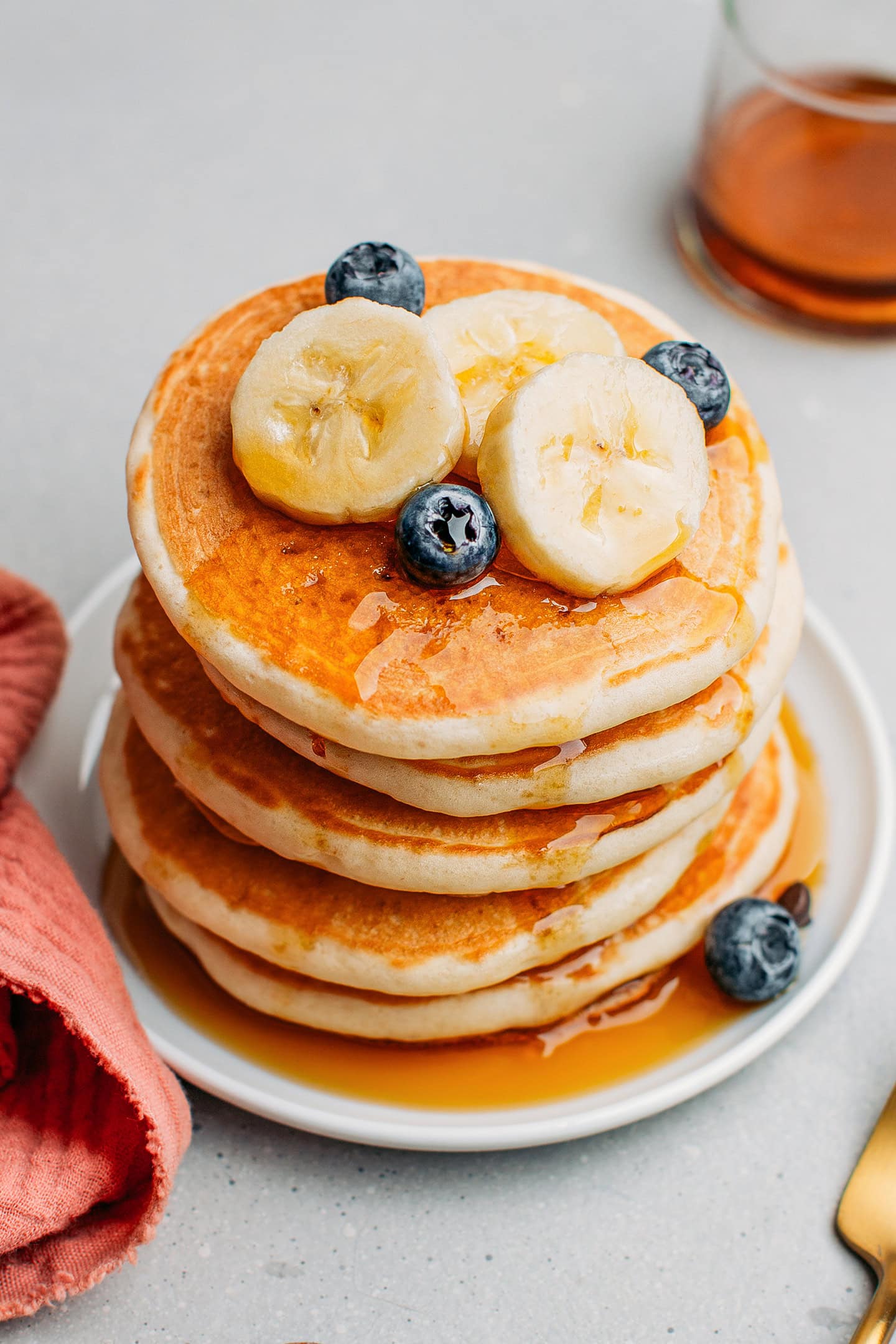 Stack of vegan pancakes drizzled with maple syrup and topped with banana slices and blueberries.