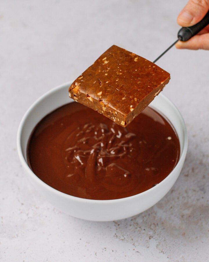 Holding a protein bar over a bowl of melted dark chocolate.