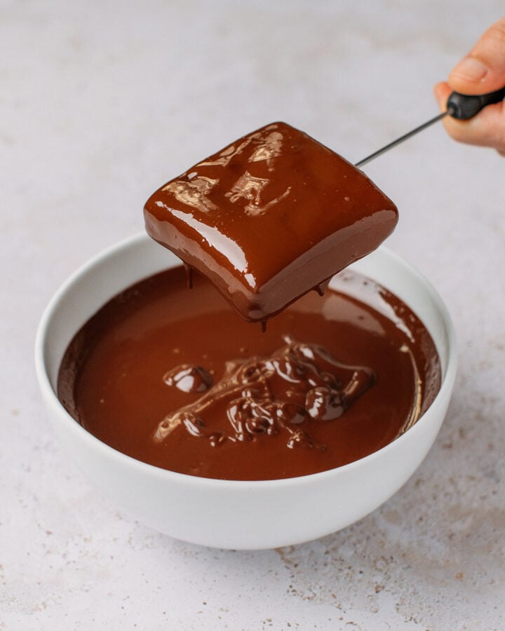 Holding a protein bar dipped in melted dark chocolate.