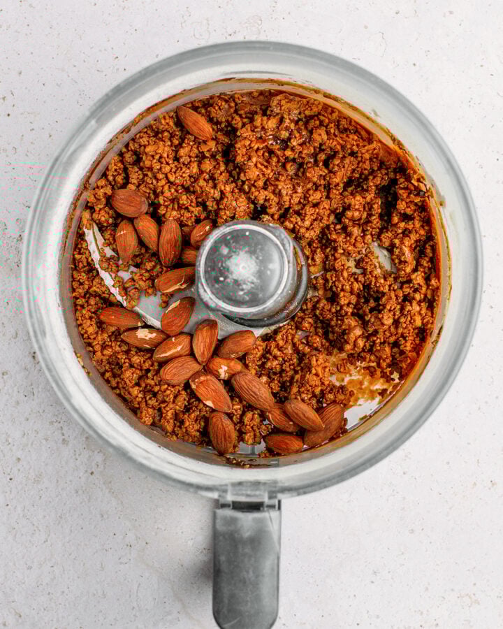 Protein bar mixture and roasted almonds in a food processor.