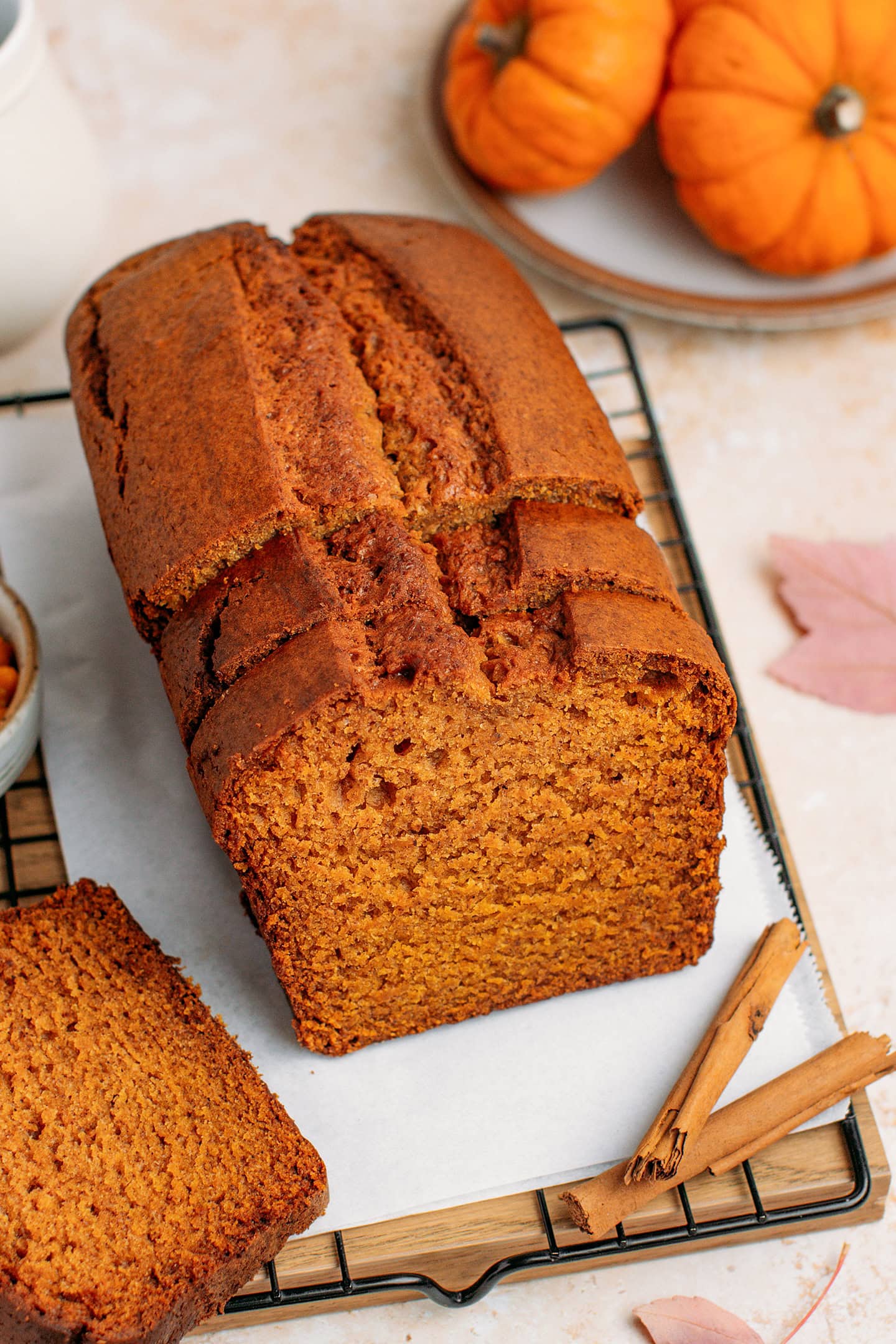Sliced pumpkin bread on a cooking rack with pumpkins in the background.