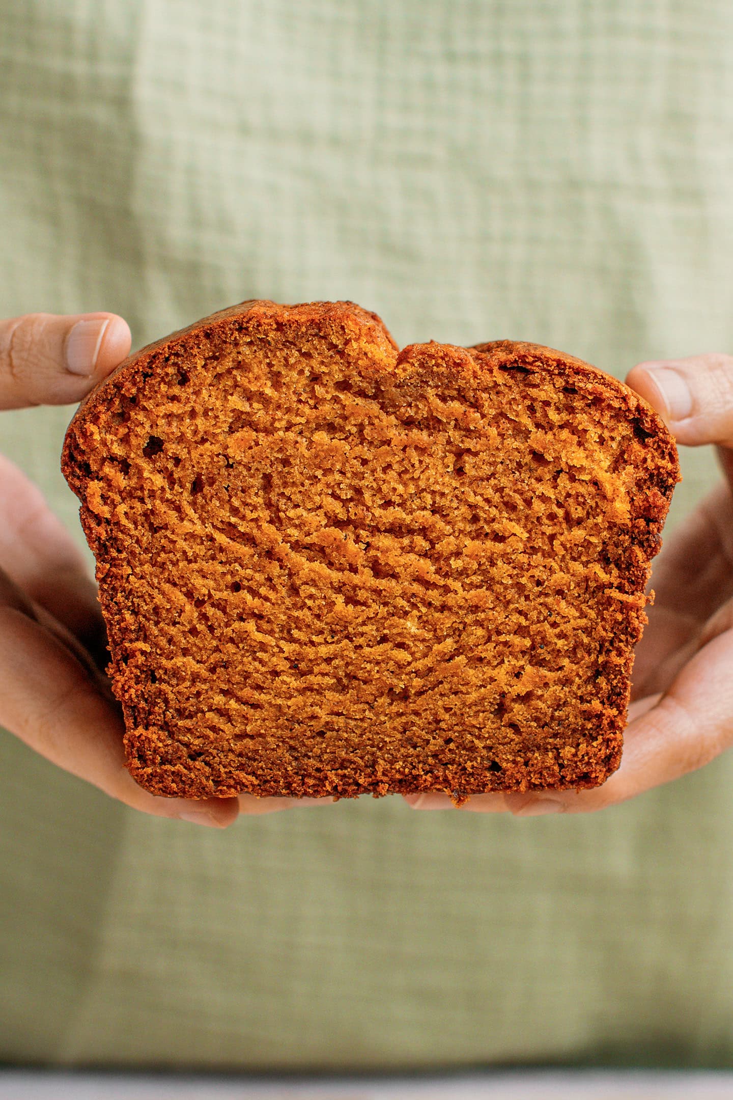 Holding a slice of pumpkin bread while wearing a green apron.