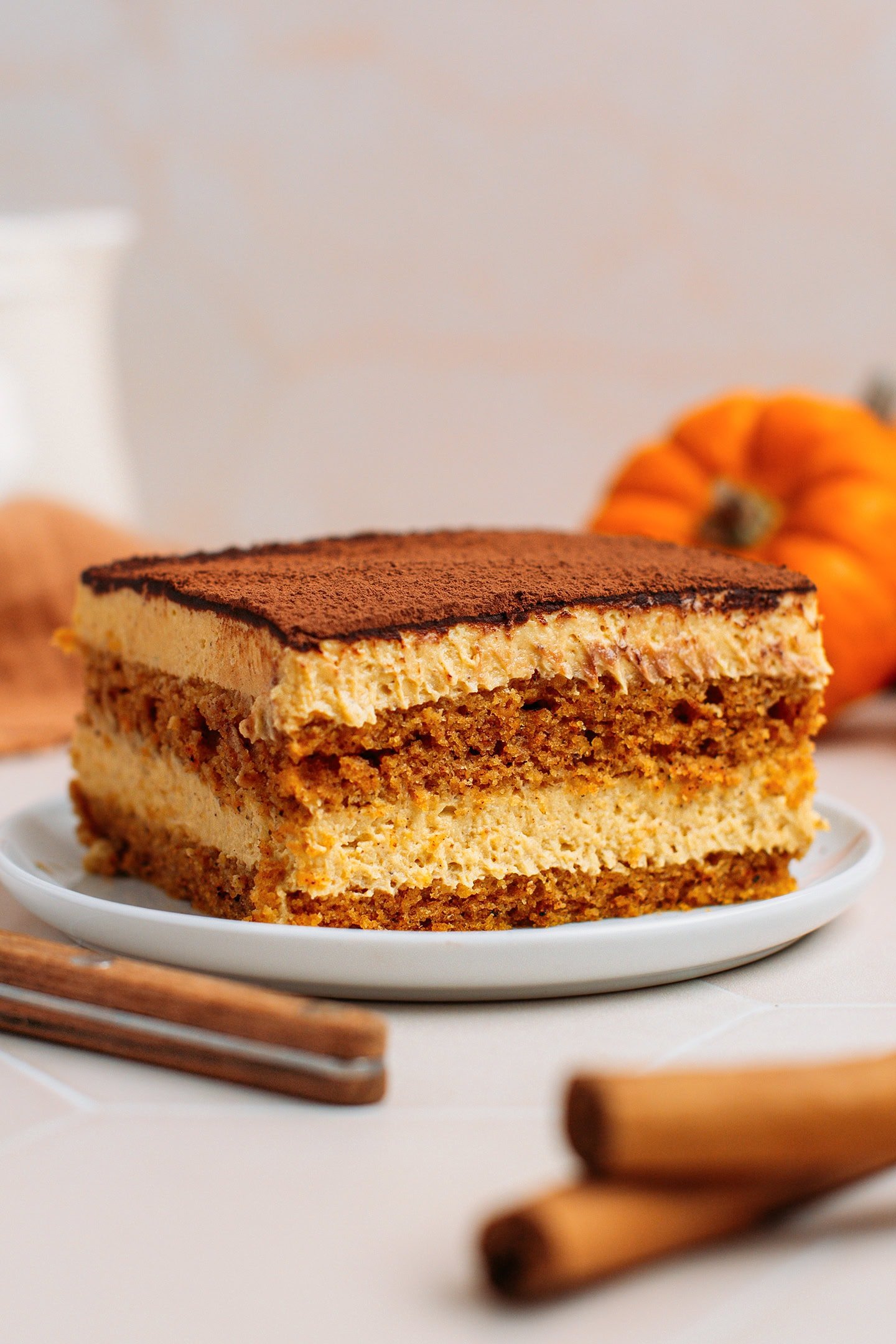 Slice of creamy pumpkin tiramisu dusted with cocoa powder on a white plate.