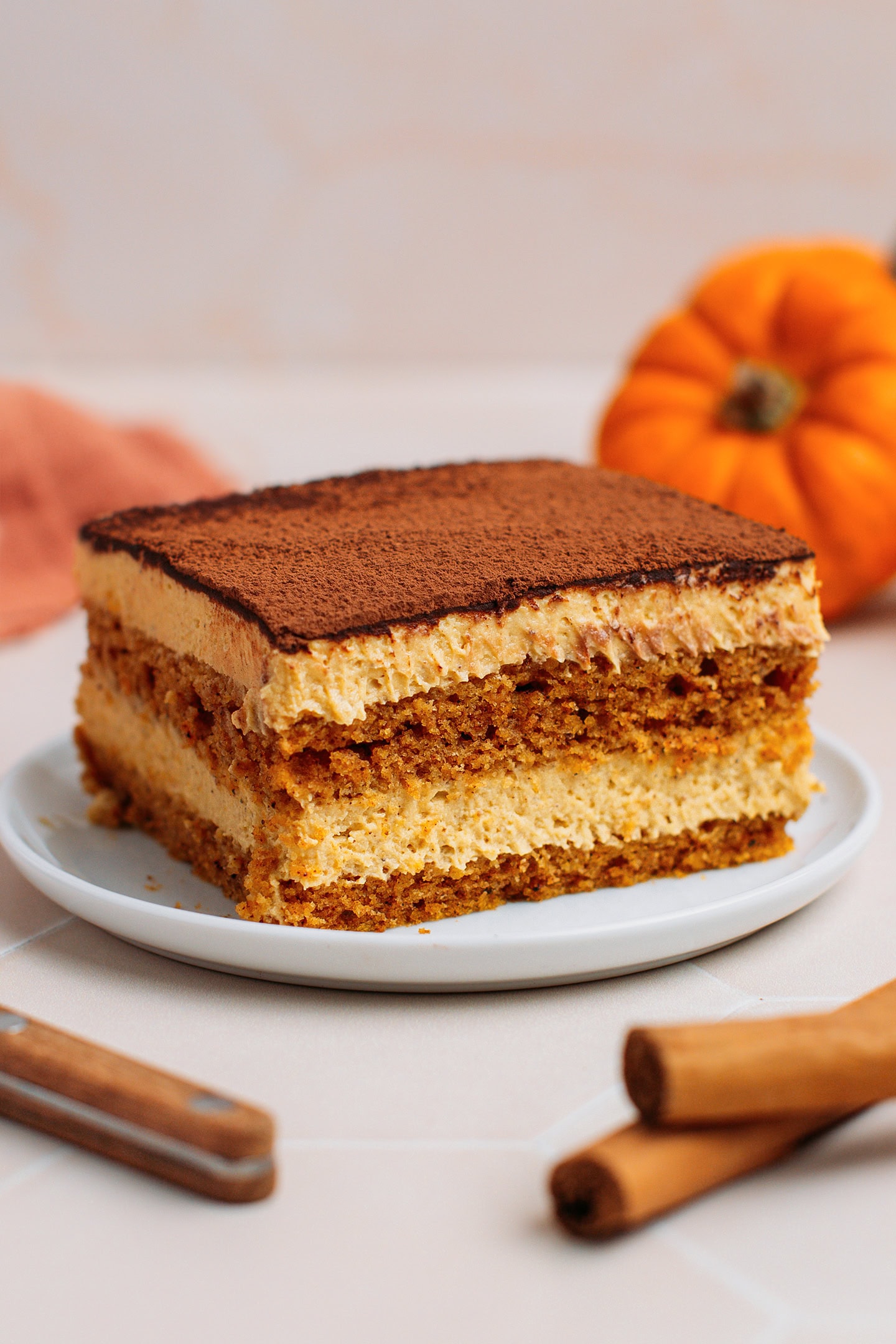Slice of pumpkin tiramisu dusted with cocoa powder on a white plate.