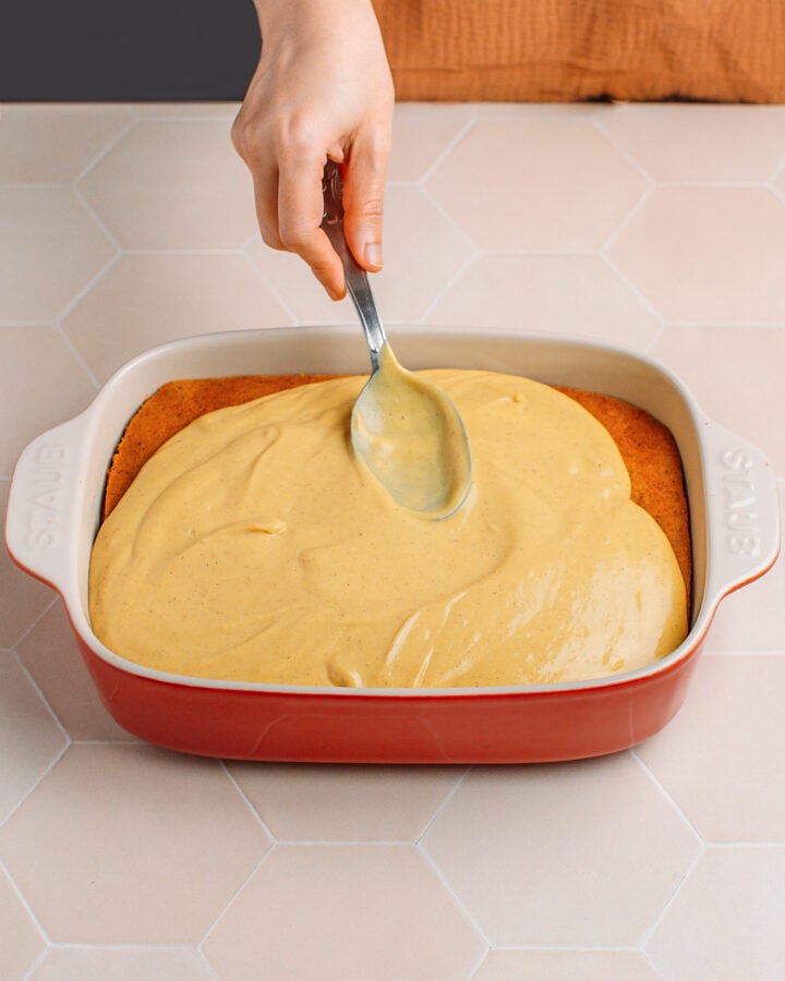 Spreading pumpkin cream over a sponge cake inside a baking dish.