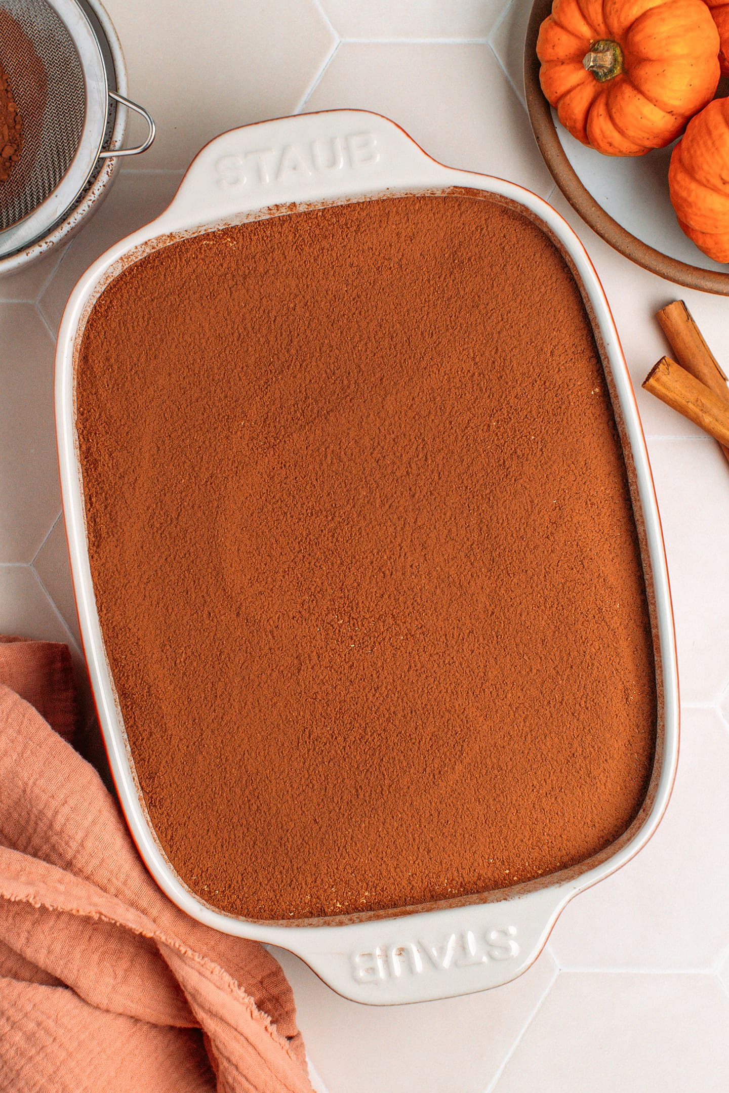 Baking dish filled with pumpkin tiramisu and dusted with cocoa powder.