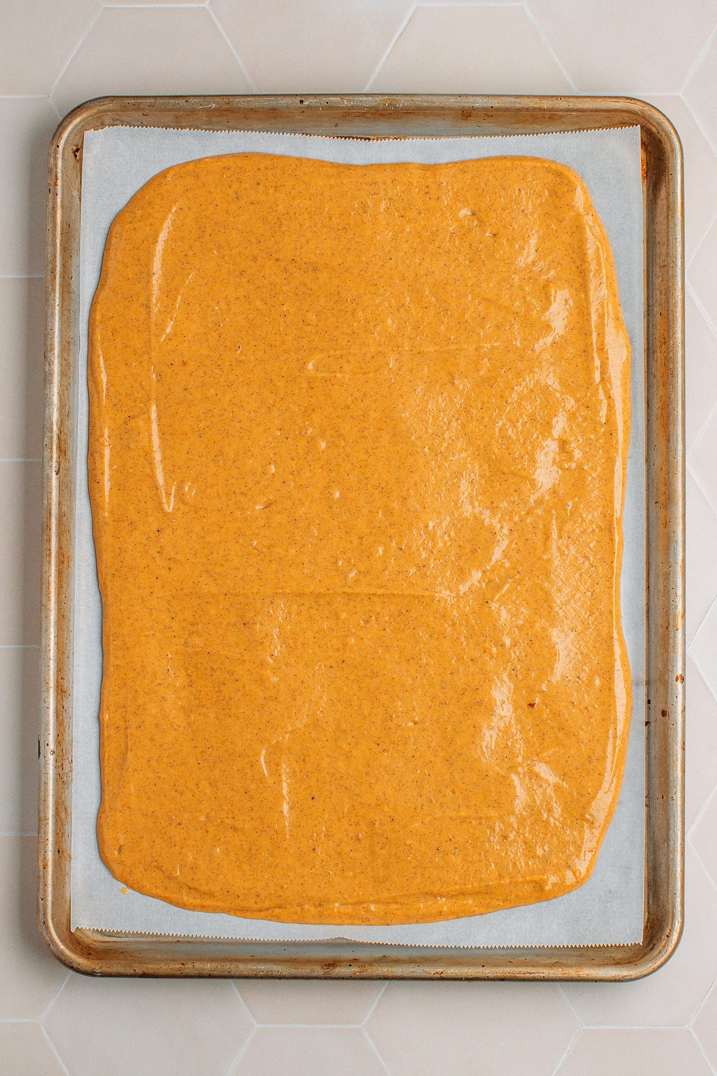 Unbaked pumpkin sponge cake spread on a baking sheet.