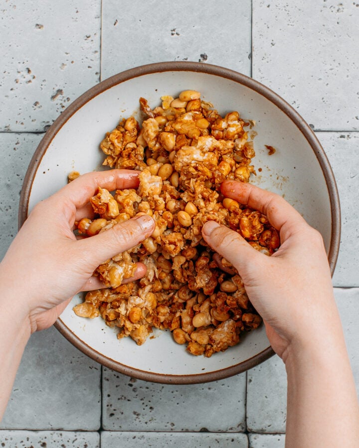 Tossing scrambled tempeh with soy sauce and sesame oil.