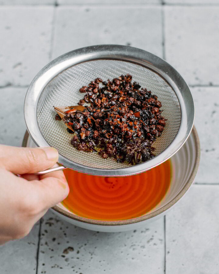 Holding a fine-mesh sieve filled with red pepper flakes over a bowl of chili oil.