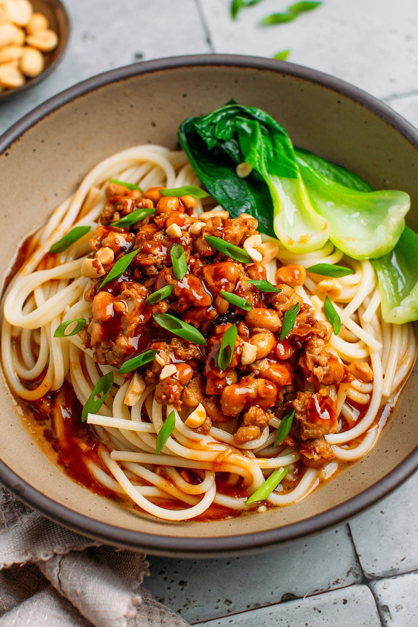Close-up shot of saucy noodles topped with scrambled tempeh, roasted peanuts, and green onions.