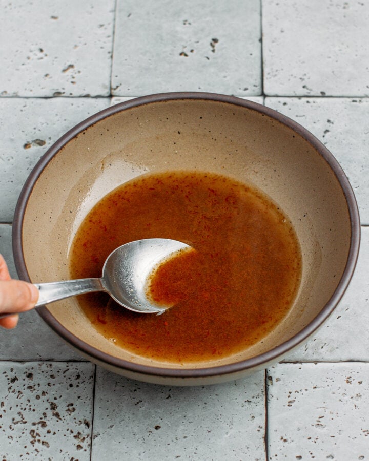 Stirring sauce with pasta water in a brown bowl.