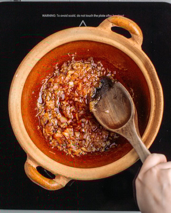 Stirring minced shallots with caramel inside a clay pot.