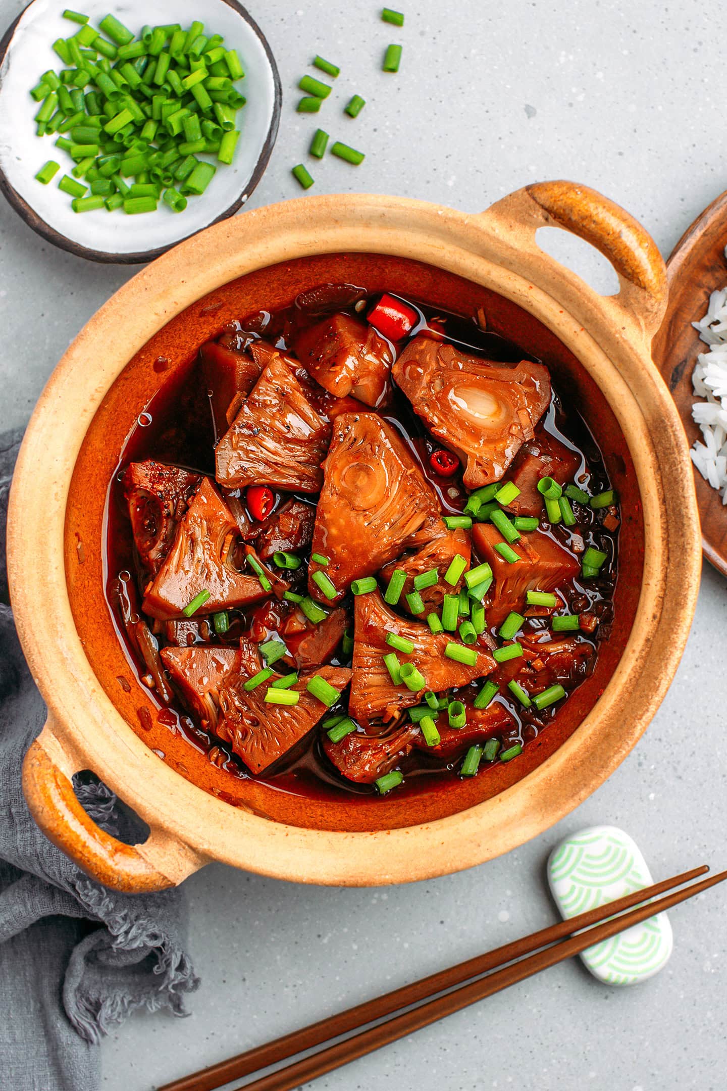 Top view of a clay pot filled with braised jackfruit topped with green onions.