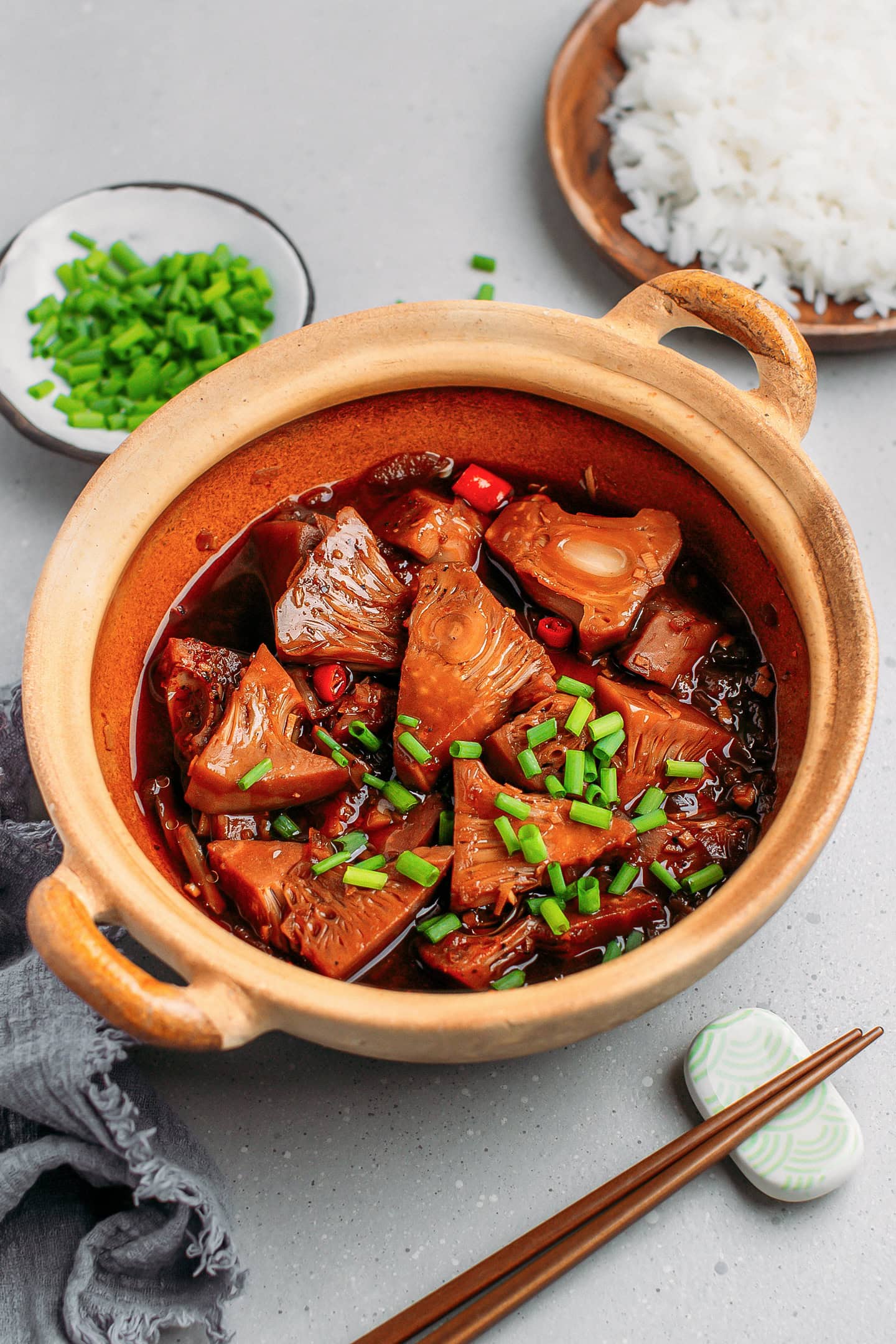 Braised jackfruit chunks topped with chopped green onions in a clay pot.