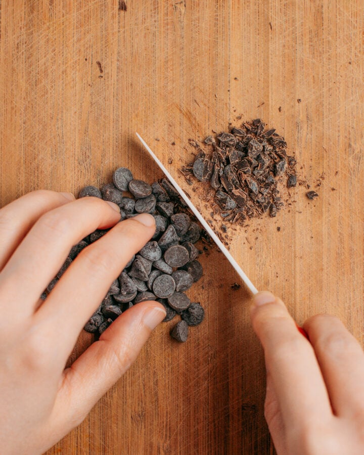 Chopping chocolate chips on a wood cutting board.