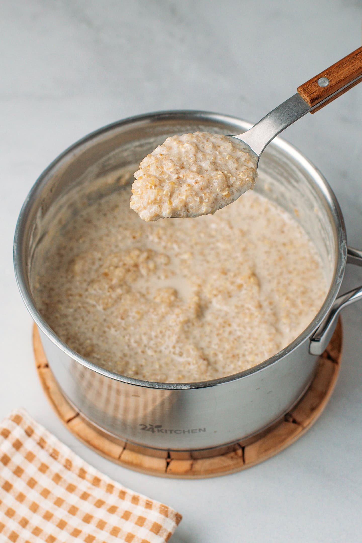 Holding a spoonful of quinoa pudding over a saucepan.