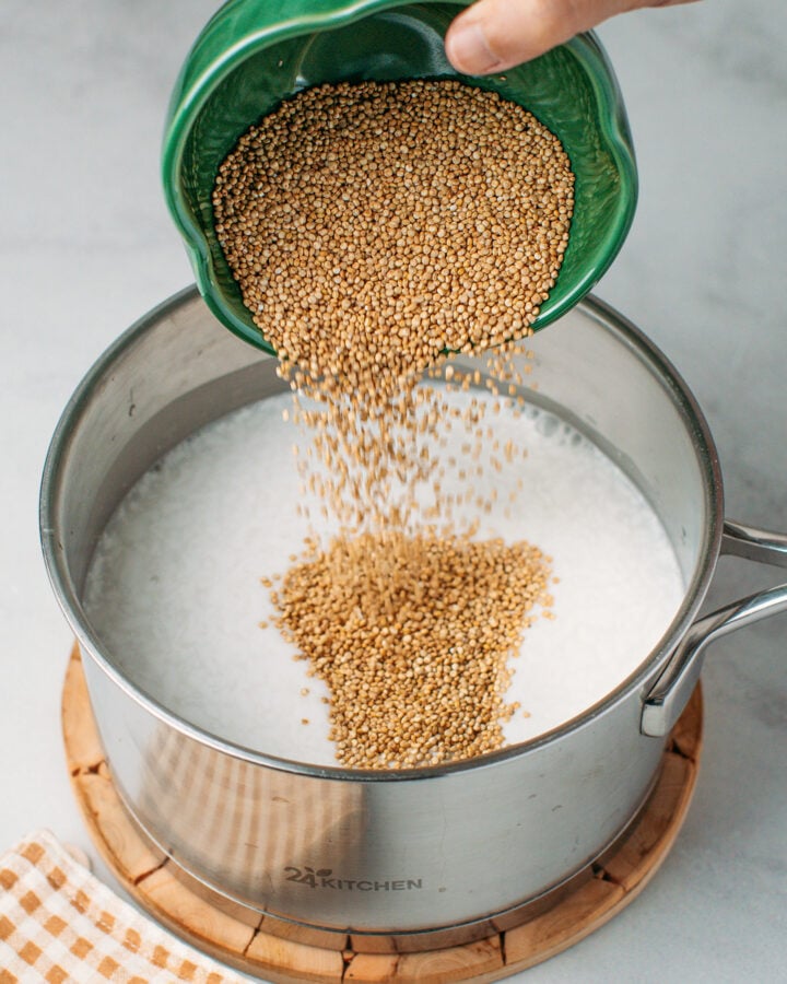 Pouring quinoa into a saucepan containing coconut milk and water.