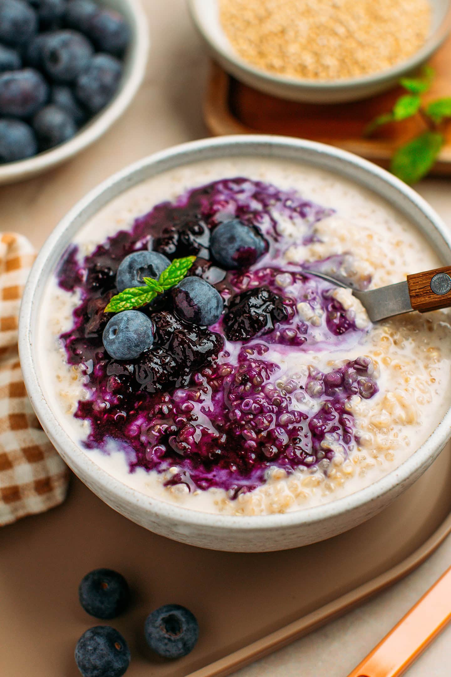 Digging a spoon into a bowl of quinoa pudding topped with blueberry compote.