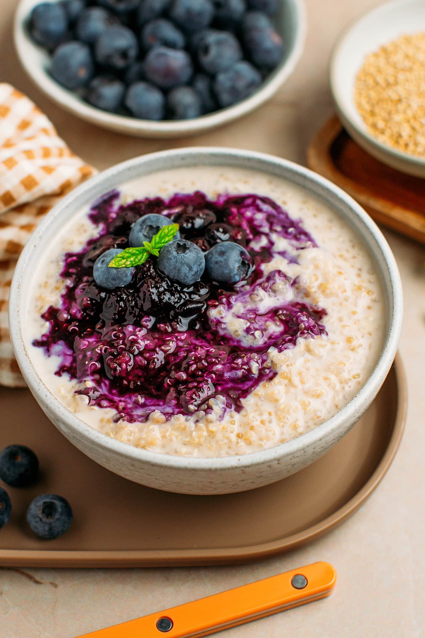 White bowl filled with quinoa pudding and topped with blueberry compote, fresh blueberries, and mint leaves.