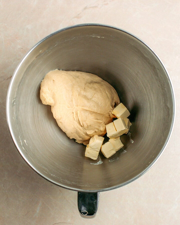 Ball of dough and cubed butter in a stand mixer bowl.