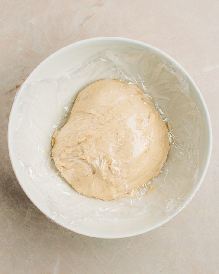 Brioche dough covered with plastic wrap in a mixing bowl.