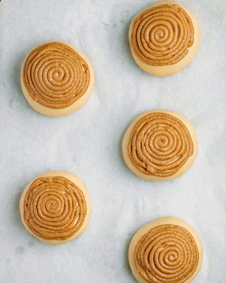 Five balls of dough covered with a coffee craquelin on a baking sheet.