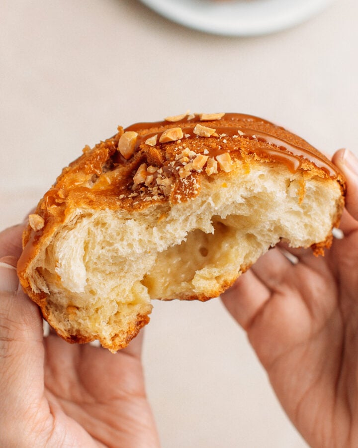 Holding a halve of a Papparoti bun topped with caramel sauce and crushed peanuts.