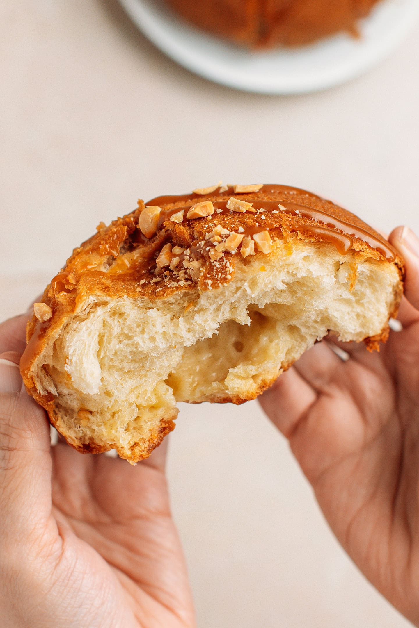 Holding a halve of a Papparoti bun topped with caramel sauce and crushed peanuts.