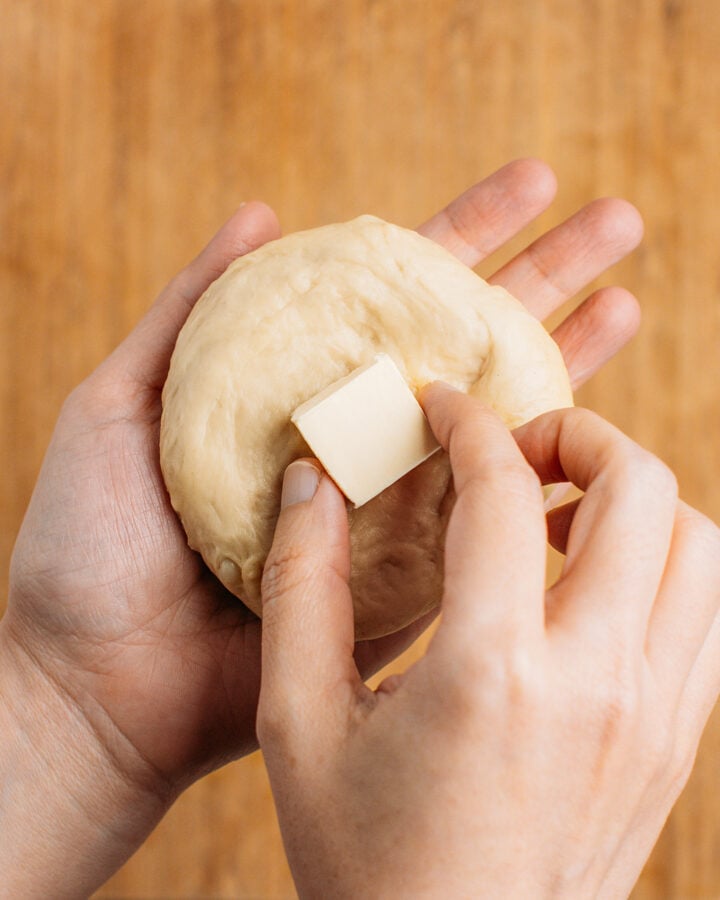 Placing a cube of butter inside a ball of dough.