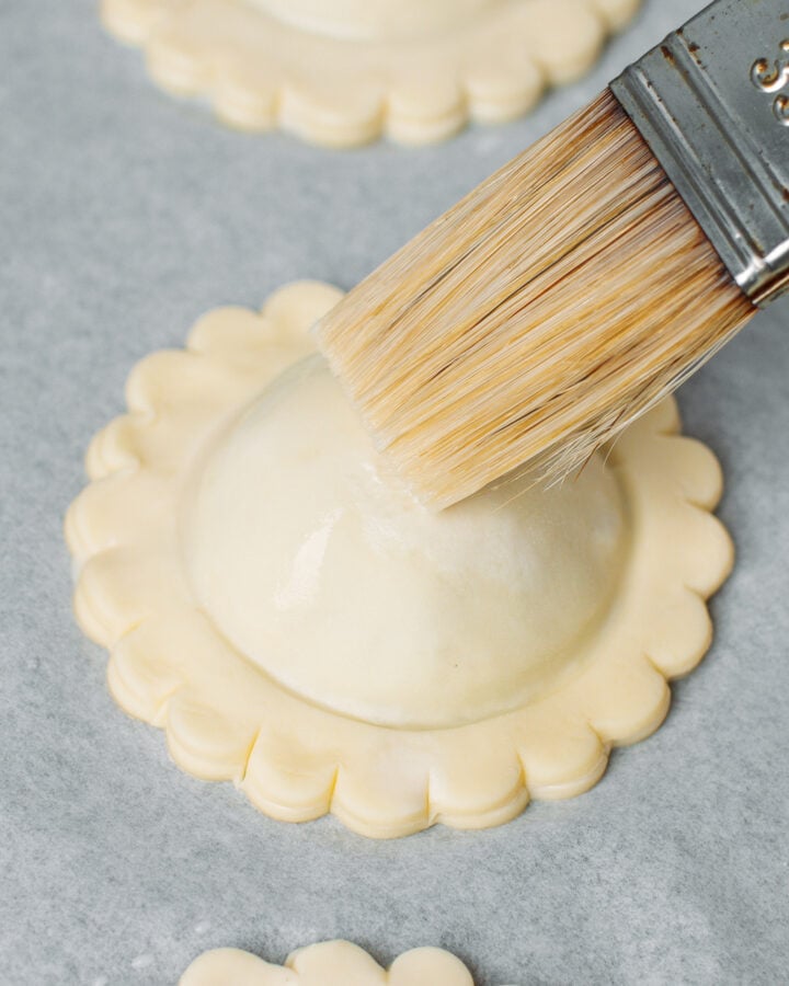Brushing an unbaked vegan meat pastry with milk.