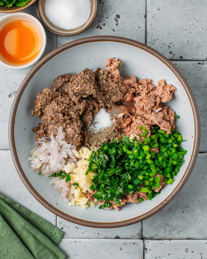 Vegan ground meat, p&acirc;t&eacute;, chopped green onions, garlic, and shallot in a mixing bowl.