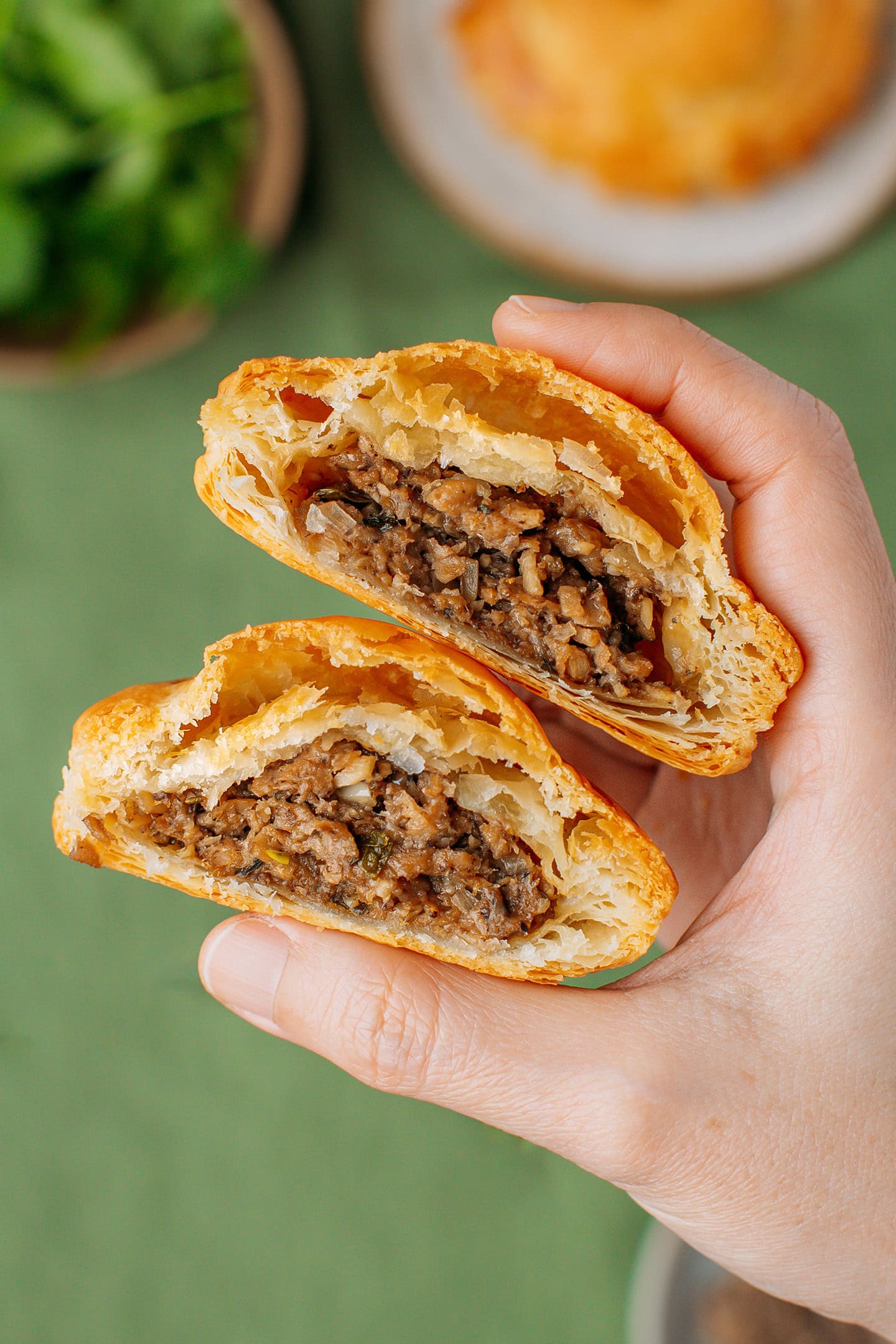 Holding two small savory pastries filled with a meaty filling.