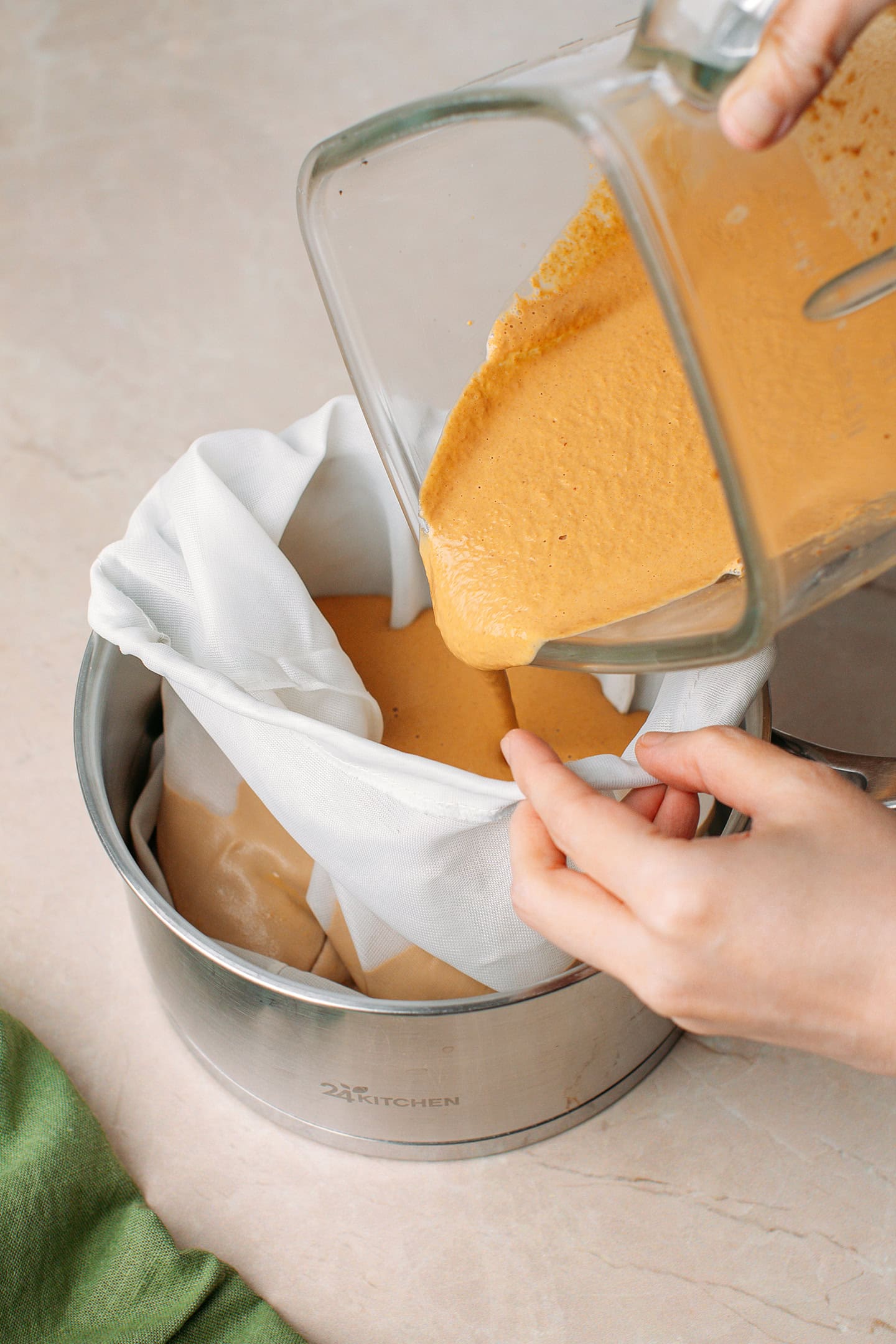 Pouring peanut milk into a nut milk bag sitting into a saucepan.