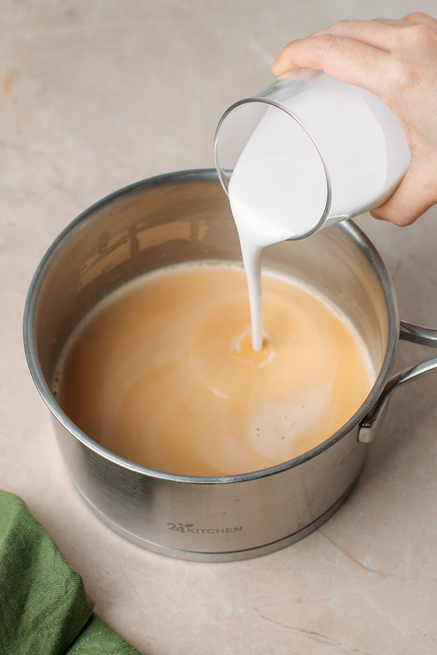 Pouring coconut milk into a saucepan containing peanut milk.