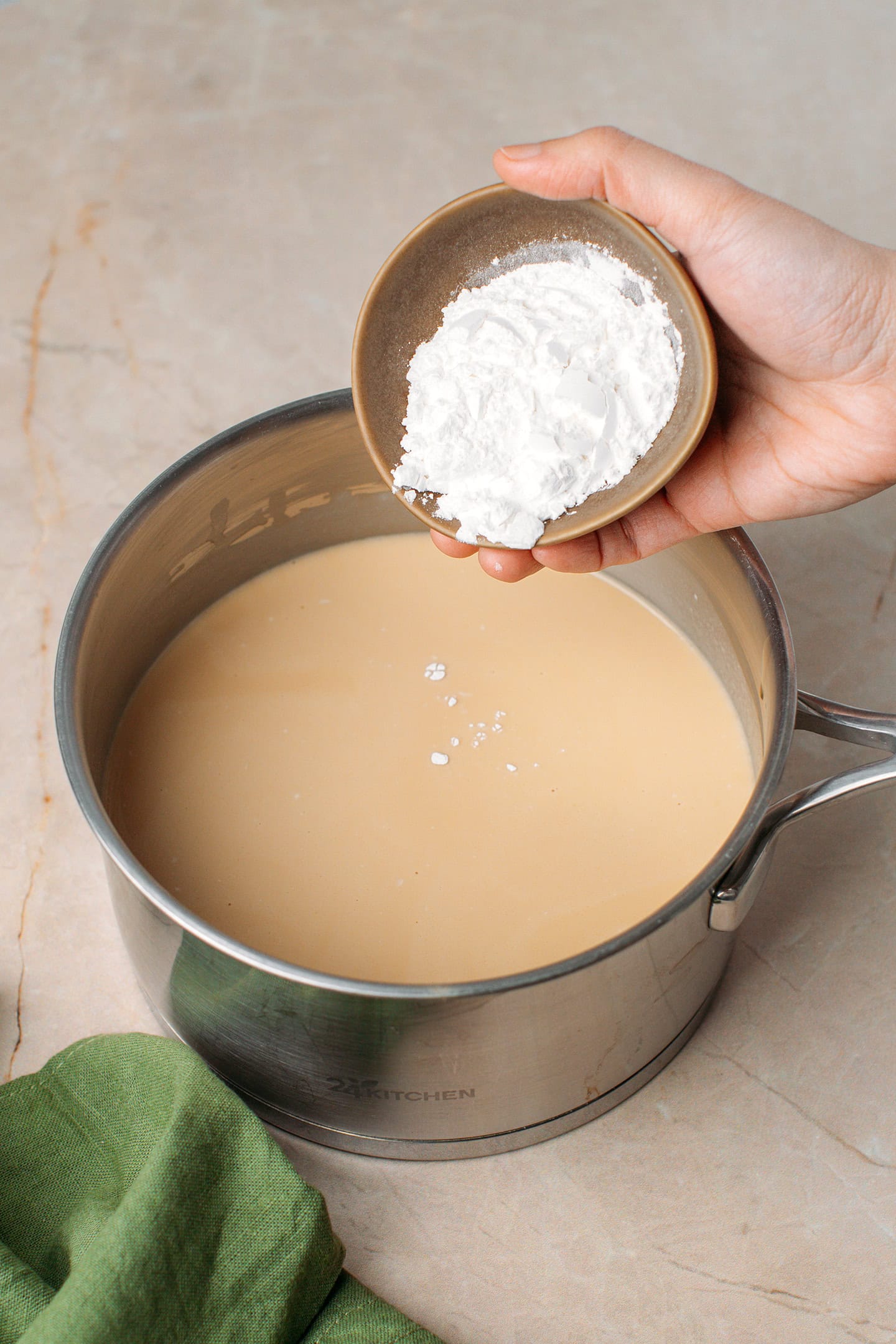Adding sweet rice flour to a saucepan containing peanut milk.