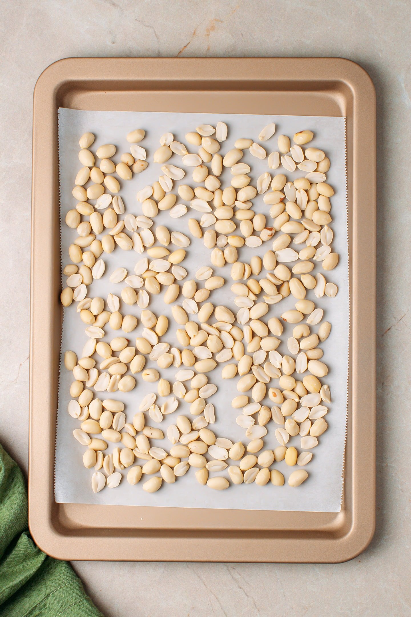 Raw peanuts arranged on a baking sheet.