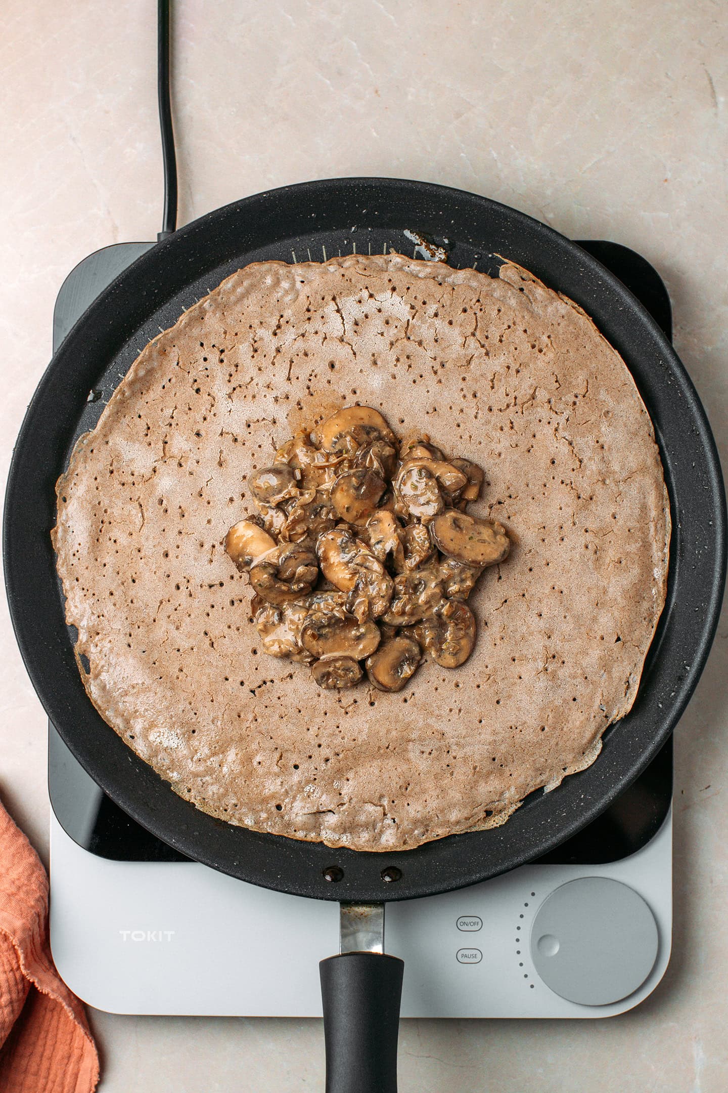 Cooked buckwheat crêpe garnished with sautéed mushrooms in a non-stick skillet.