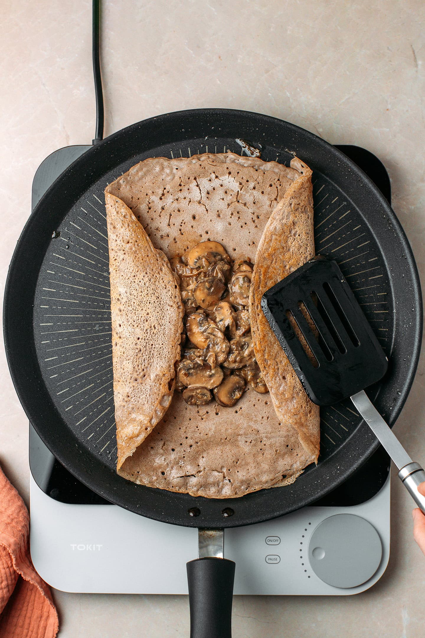 Using a spatula to fold the edges of a crêpe over a mushroom filling.