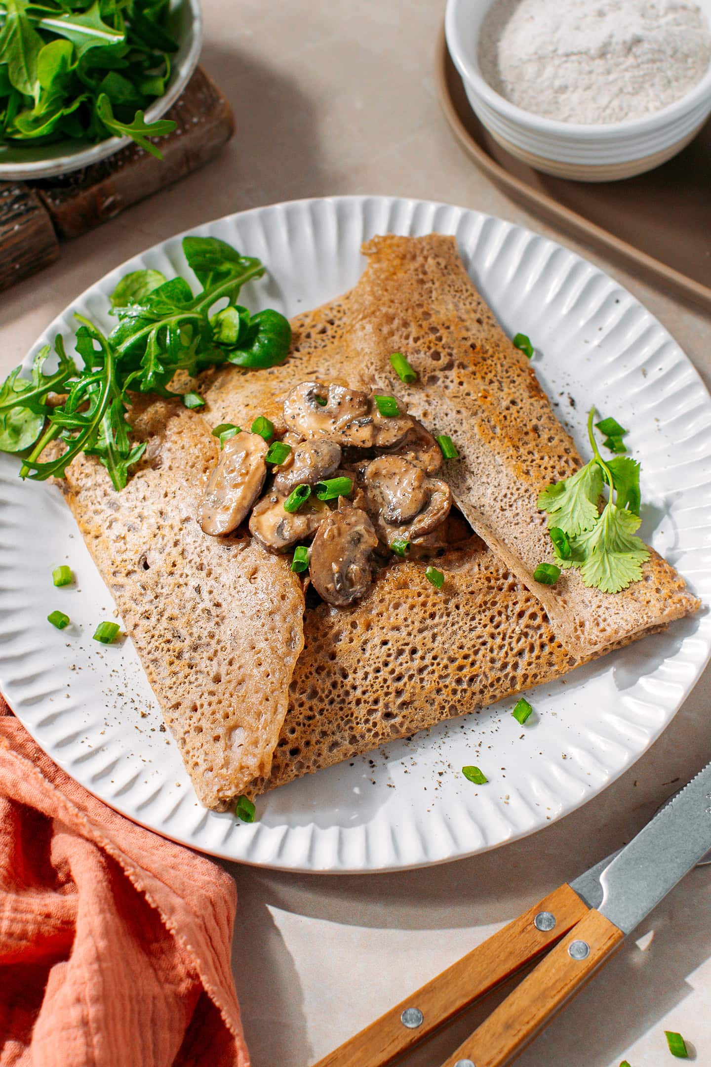 Buckwheat crêpe garnished with sautéed mushrooms on a white plate.