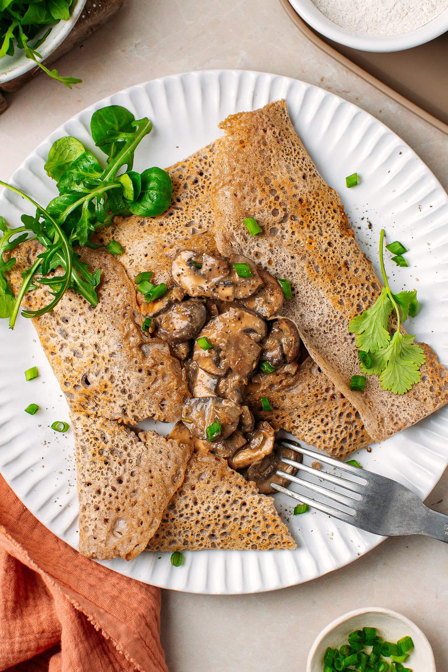 Top view of a buckwheat crêpe garnished with mushrooms and topped with chopped green onions.